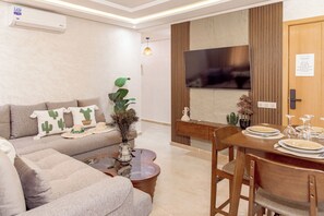 Ein modernes Wohnzimmer mit einer Couch, einem Couchtisch, einem Esstisch für vier Personen und einem an einer Holzvertäfelung montierten Flachbildfernseher.