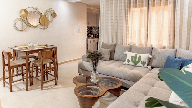 A living room with a sofa, a coffee table, and a dining area with chairs and a table. - Comfortable apartment in the heart of Guéliz (Marrakech)