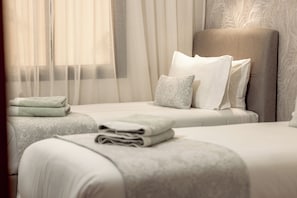 Ein Hotelzimmer mit zwei Betten, einem großen Kopfteil und durchsichtigen Vorhängen.
