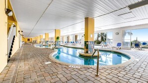 Piscina interior com pavimento ladrilhado, cadeiras de descanso e vista desimpedida para o exterior.