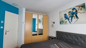 Une chambre à coucher comprenant un lit, une armoire, une table de chevet et un tableau représentant des oiseaux accroché au mur.