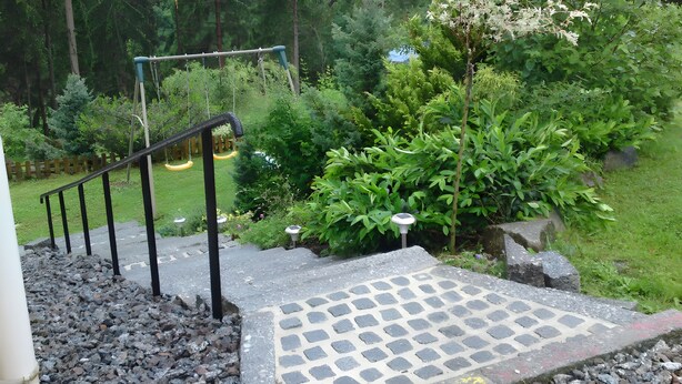 Un escalier en béton avec des rampes noires menant à une zone pavée ornée d’un motif décoratif.