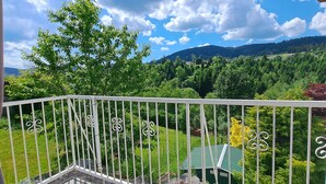 Un balcon avec une balustrade blanche, donnant sur un paysage verdoyant avec des arbres et une montagne en arrière-plan.
