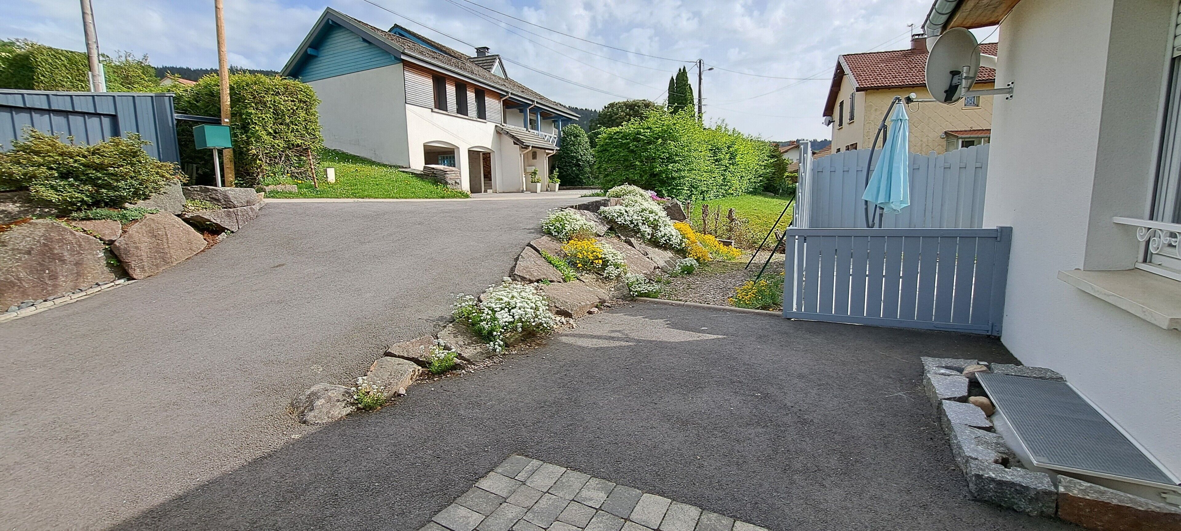 A residential street with houses, a gated driveway, and a clear sky.