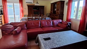 Un salon avec un canapé en cuir rouge, une table à manger avec des chaises, un buffet et un luminaire au plafond.
