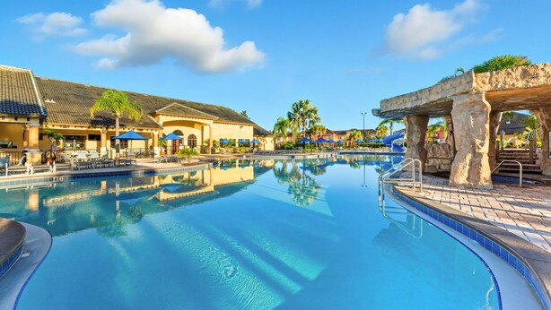 Une piscine à l’eau d’un bleu limpide, entourée de chaises longues et de parasols, avec des bâtiments en arrière-plan.