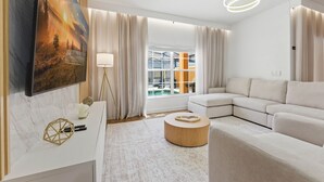 Un salon moderne avec un canapé d’angle, une table basse ronde, un tableau et une grande fenêtre avec des rideaux.