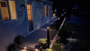 Une maison avec une terrasse en bois, des plantes en pot et une entrée éclairée.