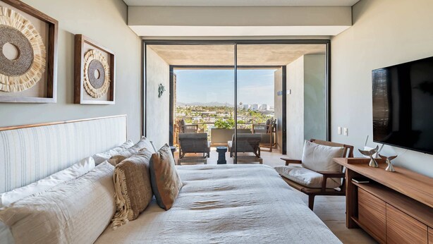 Quarto moderno com uma cama grande, televisão e varanda com vista para a cidade.