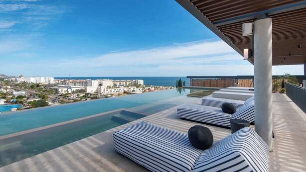 A rooftop infinity pool with striped lounge chairs and a view of the city and ocean. - Punto Nima: Panoramic PH with Private Terrace (San José del Cabo)
