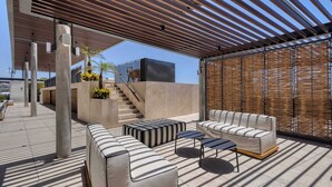 An outdoor seating area with modern furniture, a staircase, and a covered section with a wooden slatted roof. - Punto Nima: Panoramic PH with Private Terrace (San José del Cabo)