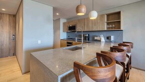 A modern kitchen with a central island, wooden chairs, pendant lights, and built-in shelves. - Punto Nima: Panoramic PH with Private Terrace (San José del Cabo)