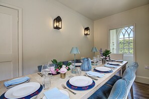 A dining room with a long table set for six, two wall-mounted light fixtures, and a window with a view of greenery. - Beautiful House for 8 set in idyllic Audley End - with hot tub and cosy fire (Audley End)