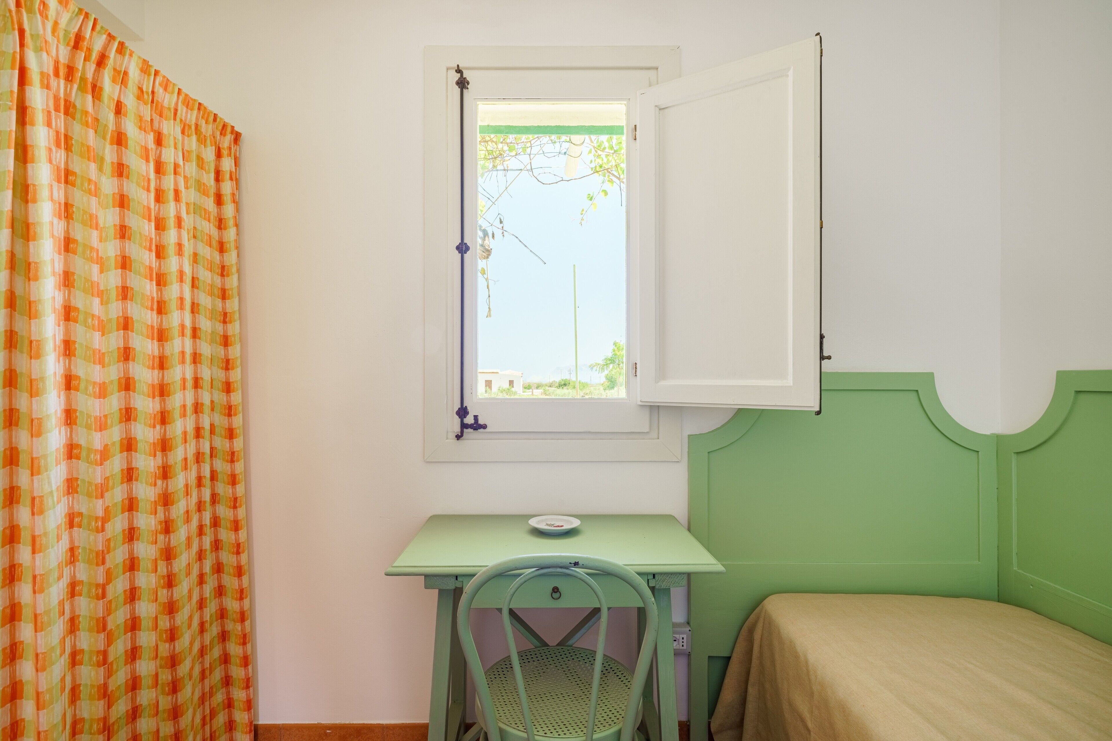 Een kamer met een bed, een tafel met stoel, een raam met gordijnen en een deur.