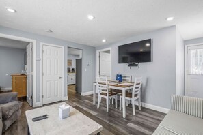 Una sala de estar con televisor, mesa de comedor con sillas, sofá y mesa de centro.