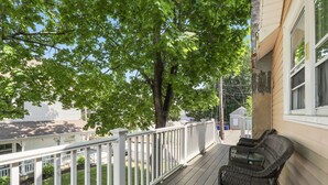 En træterrasse med hvide gelændere, fletmøbler og et træ, der giver skygge.