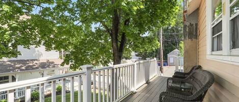 A wooden deck with white railings, wicker furniture, and a tree providing shade.
