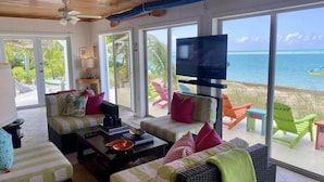 Quarto com sofá, cadeiras, televisão e vista para o oceano.