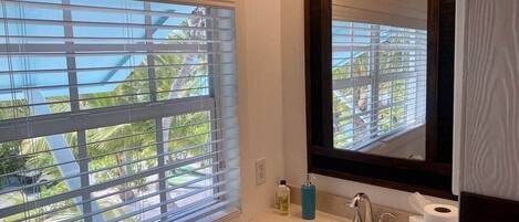 A bathroom with a window, sink, mirror, and toiletries.