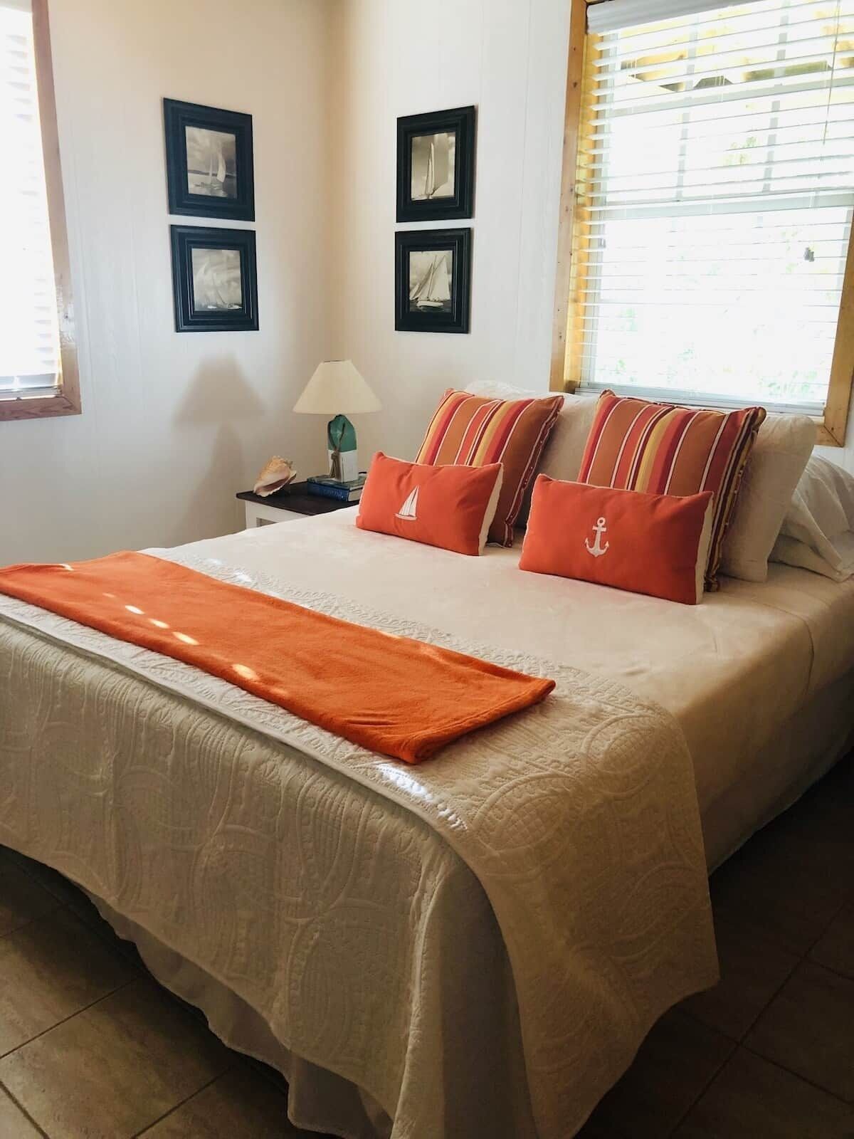 Una cama bien hecha con una colcha blanca y naranja, dos almohadas con diseños a rayas y una manta naranja a juego.
