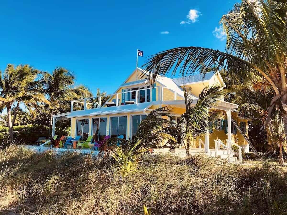 Une maison à deux étages dotée d’un balcon, entourée de palmiers et surplombant un ciel d’un bleu limpide.