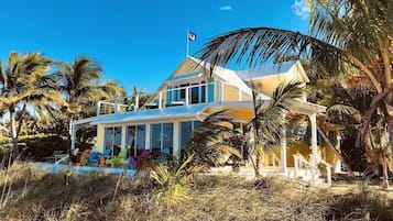 Une maison à deux étages dotée d’un balcon, entourée de palmiers et surplombant un ciel d’un bleu limpide.
