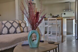 A living room with a sofa, a coffee table with a vase, and a kitchen area in the background.