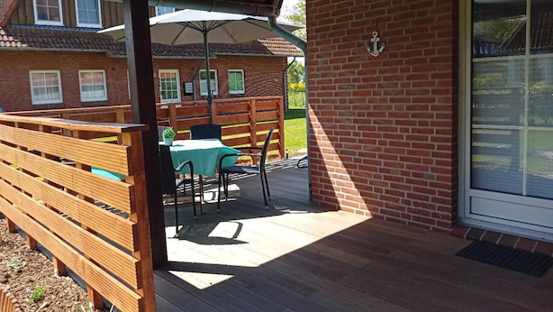 A covered patio with a table and chairs, a wooden bench, and a brick wall with a window. - Komfortable Ferienwohnung in Wenkendorf (Fehmarn)