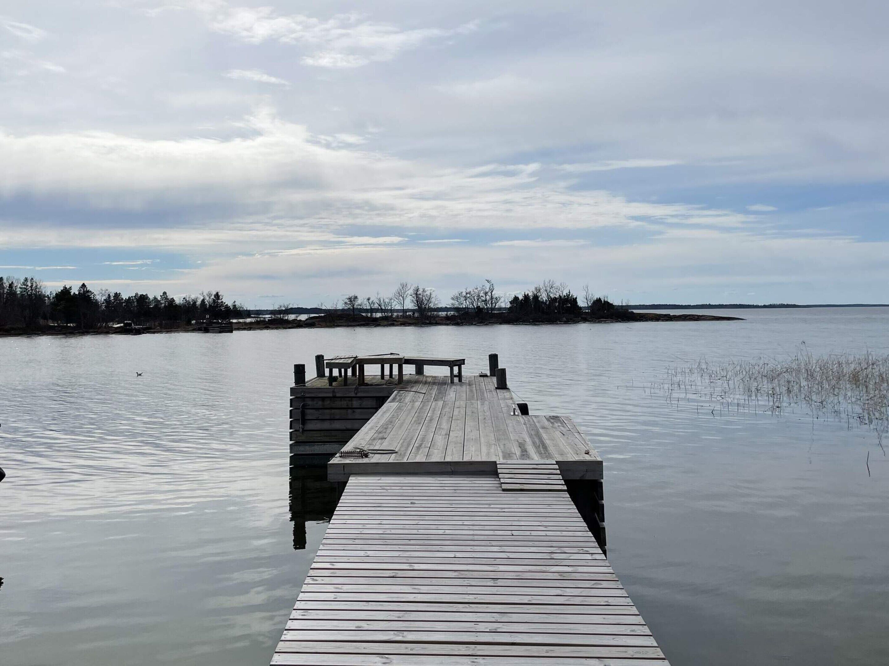 Eine Holzstele ragt in ruhiges Wasser, darüber ein bewölkter Himmel.