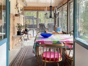 A dining area with a table, chairs, a chandelier, and a view through large windows.
