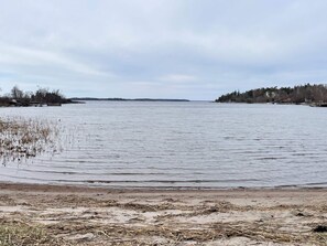 Um lago calmo com margem arenosa e vegetação escassa.