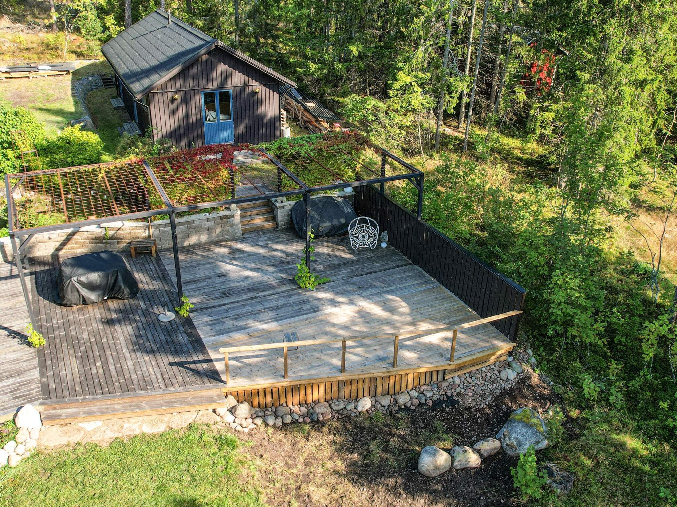 A wooden deck with a covered seating area, surrounded by a natural forest setting.