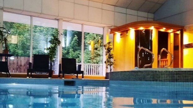 An indoor swimming pool with clear blue water, a sunlit area with a small stage, and a view of greenery outside. - Large house Drymen Village with Health club access (Drymen)