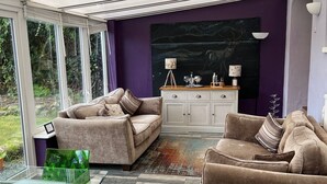 A modern living room with a glass table, two sofas, a cabinet, and a view of greenery through large windows. - Large house Drymen Village with Health club access (Drymen)