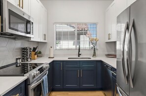 A modern kitchen with white cabinets, a stainless steel refrigerator, and a window with blinds. - Serene TPC Gem | Dining & Shopping Nearby+Walkable (Scottsdale)