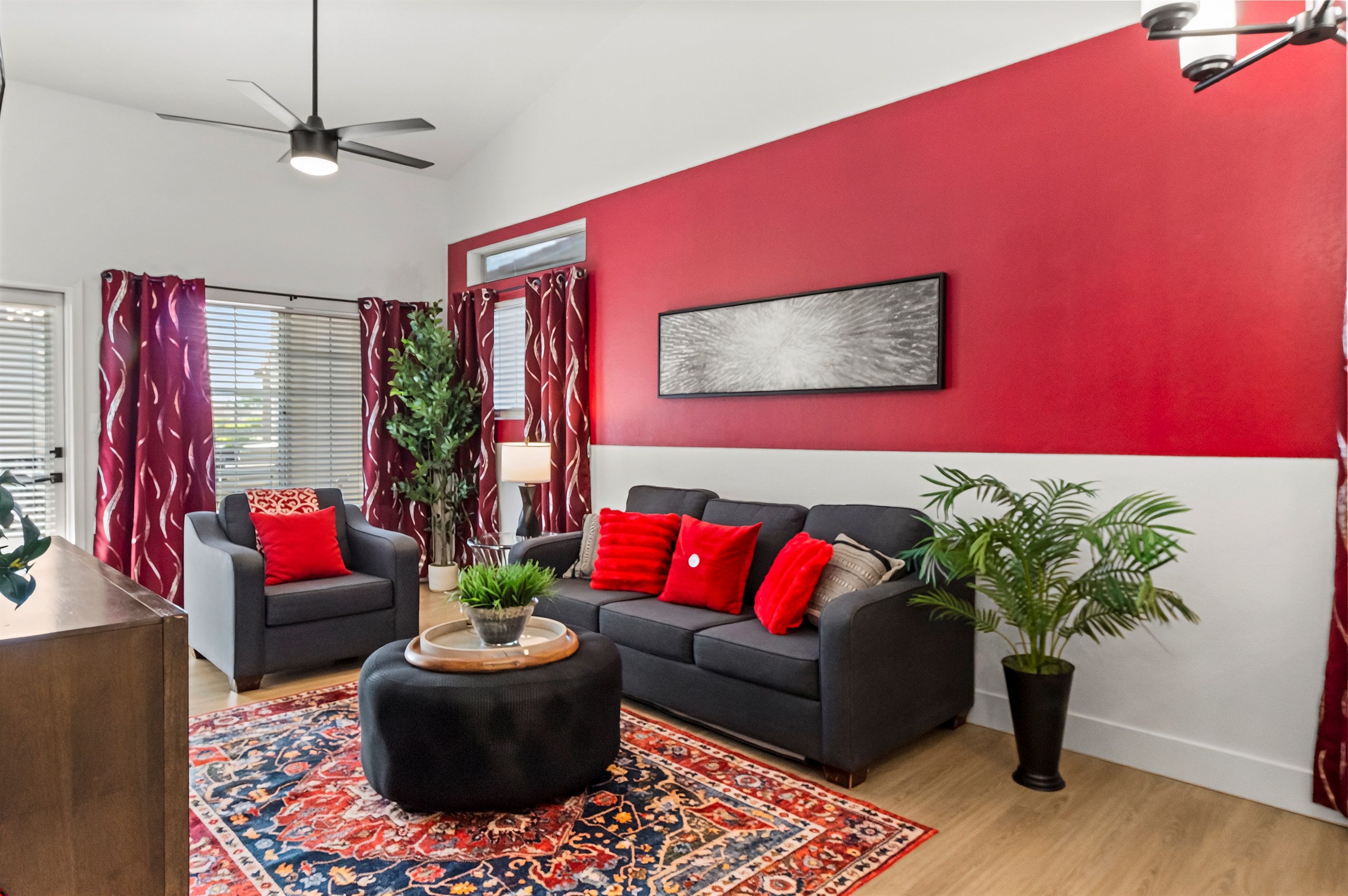 A living room with a black sofa, red cushions, a coffee table, and a red accent wall.