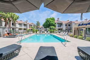 A swimming pool with lounge chairs and umbrellas, surrounded by multi-story buildings with balconies. - Serene TPC Gem | Dining & Shopping Nearby+Walkable (Scottsdale)