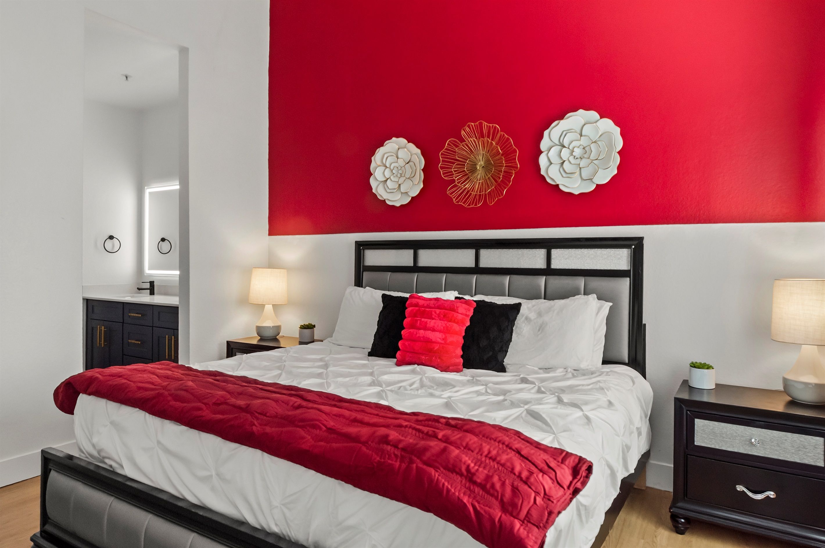 A modern bedroom with a red accent wall, a bed with white and red bedding, and decorative wall art.