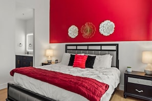 A modern bedroom with a red accent wall, a bed with white and red bedding, and decorative wall art. - Serene TPC Gem | Dining & Shopping Nearby+Walkable (Scottsdale)
