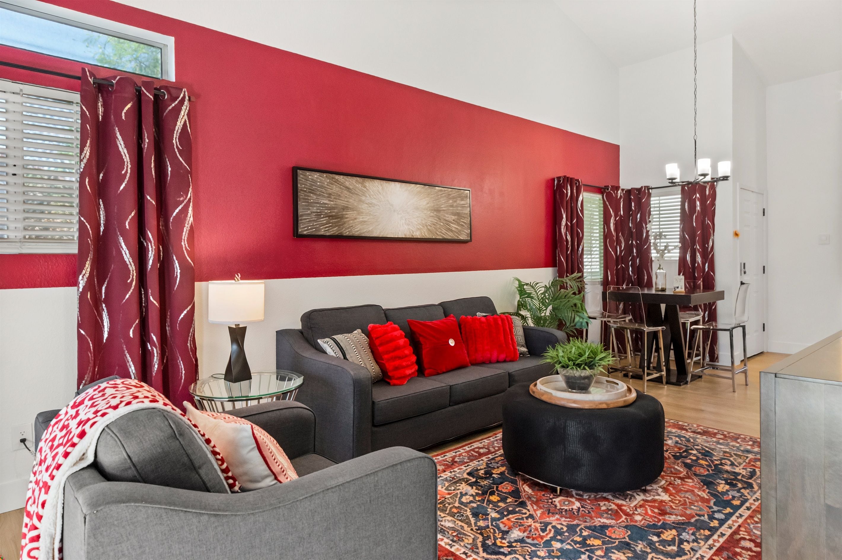 A modern living room with a red accent wall, a grey sofa, red cushions, a glass side table, and a patterned rug.