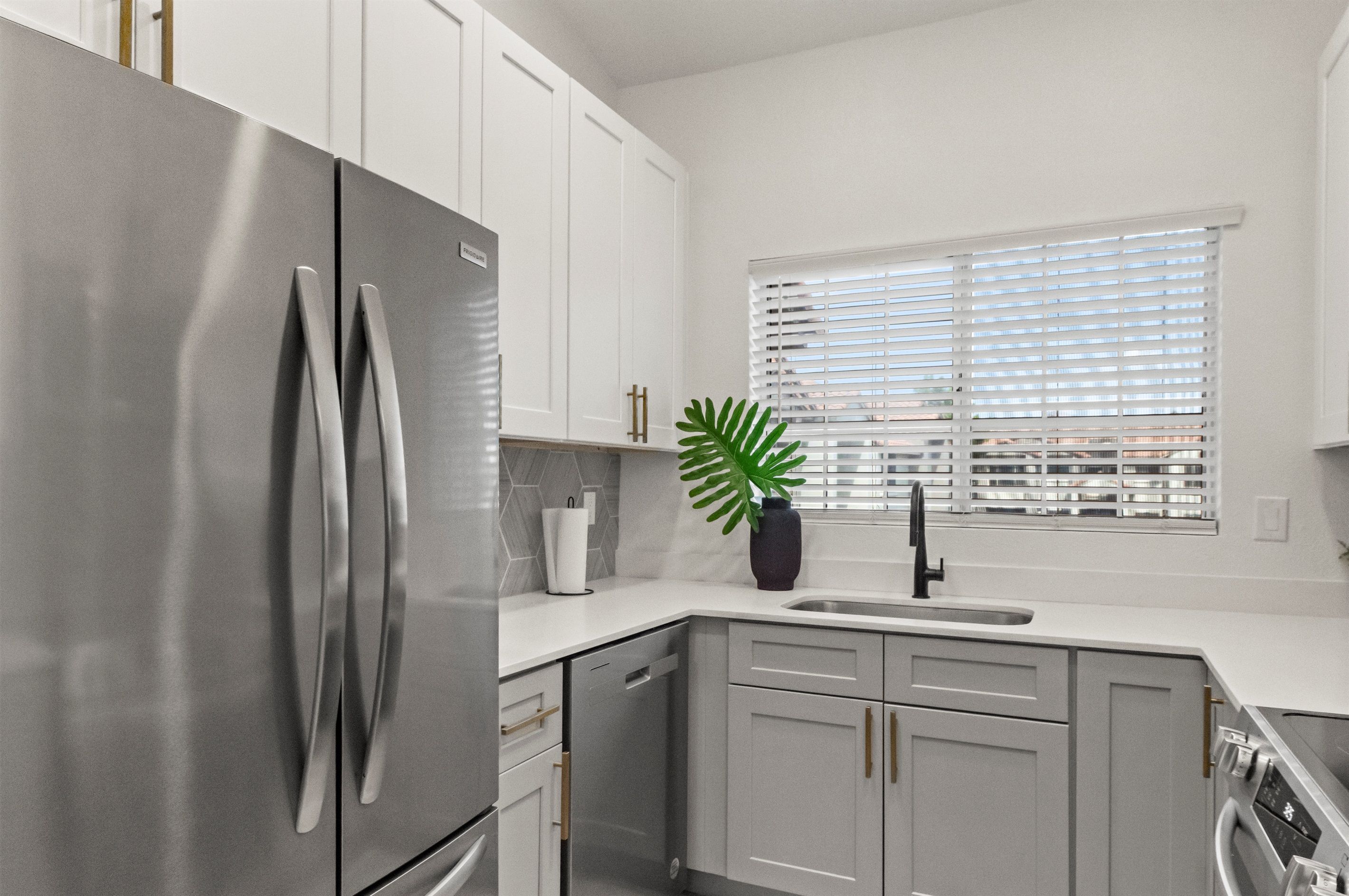 A modern kitchen with stainless steel appliances, white cabinetry, and a window with blinds.