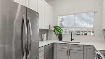 A modern kitchen with stainless steel appliances, white cabinetry, and a window with blinds.