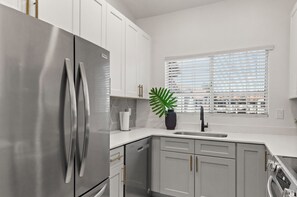 A modern kitchen with stainless steel appliances, white cabinetry, and a window with blinds. - Remodeled EnSuite Near Mayo Clinic & Barrett-Jackson (Scottsdale)