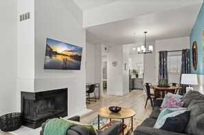 A modern living room with a fireplace, a dining area, and a kitchen visible through an open door. - Remodeled EnSuite Near Mayo Clinic & Barrett-Jackson (Scottsdale)