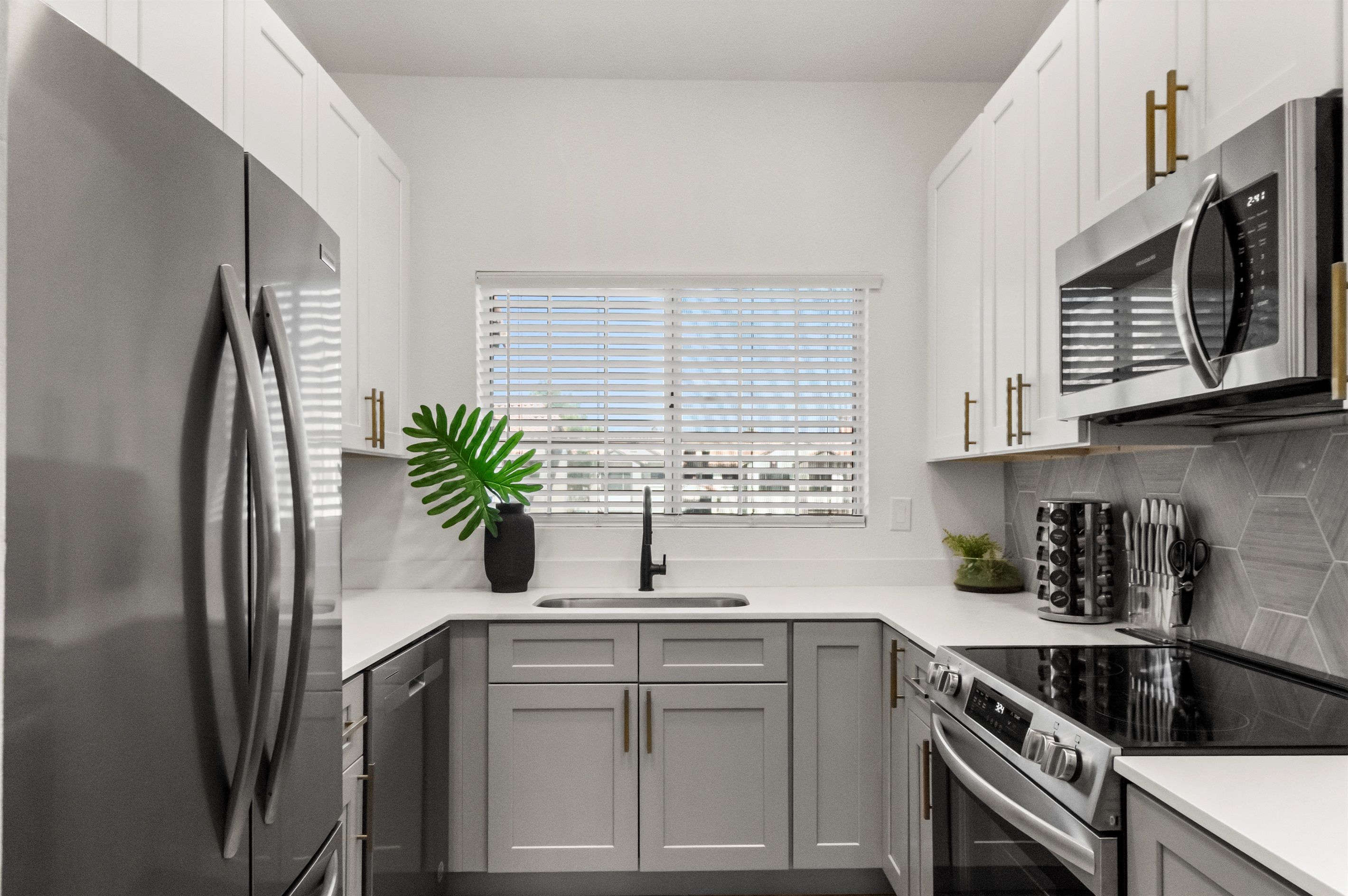 A modern kitchen with white cabinets, a stainless steel refrigerator, a built-in oven, and a microwave.