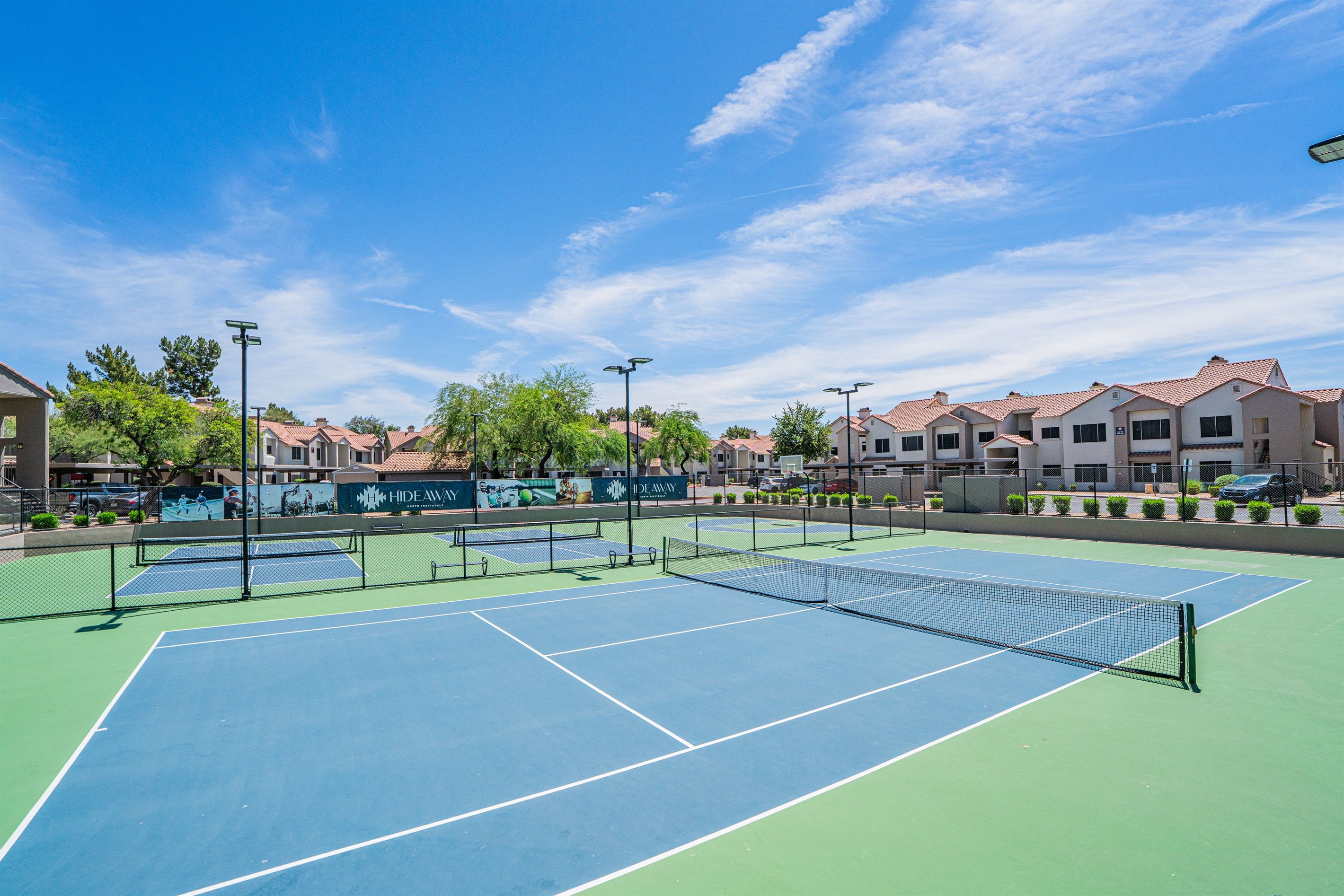 Una cancha de tenis con varias canchas, rodeada de edificios y árboles.