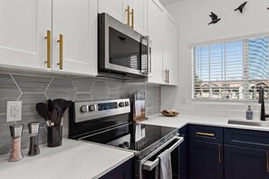 Una cocina moderna con estufa de acero inoxidable, microondas y ventana con persianas.