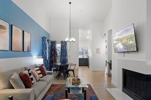 A modern living room with a sofa, coffee table, and fireplace. There is a dining area with a chandelier and a kitchen in the background. - Upscale Gourmet Retreat | Fully Stocked kitchen (Scottsdale)
