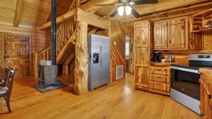 Interior de una cabaña de madera con escalera de madera, refrigerador, estufa y zona de cocina.