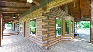 Una cabaña de troncos con terraza de madera, ventanas amplias y ventiladores de techo.